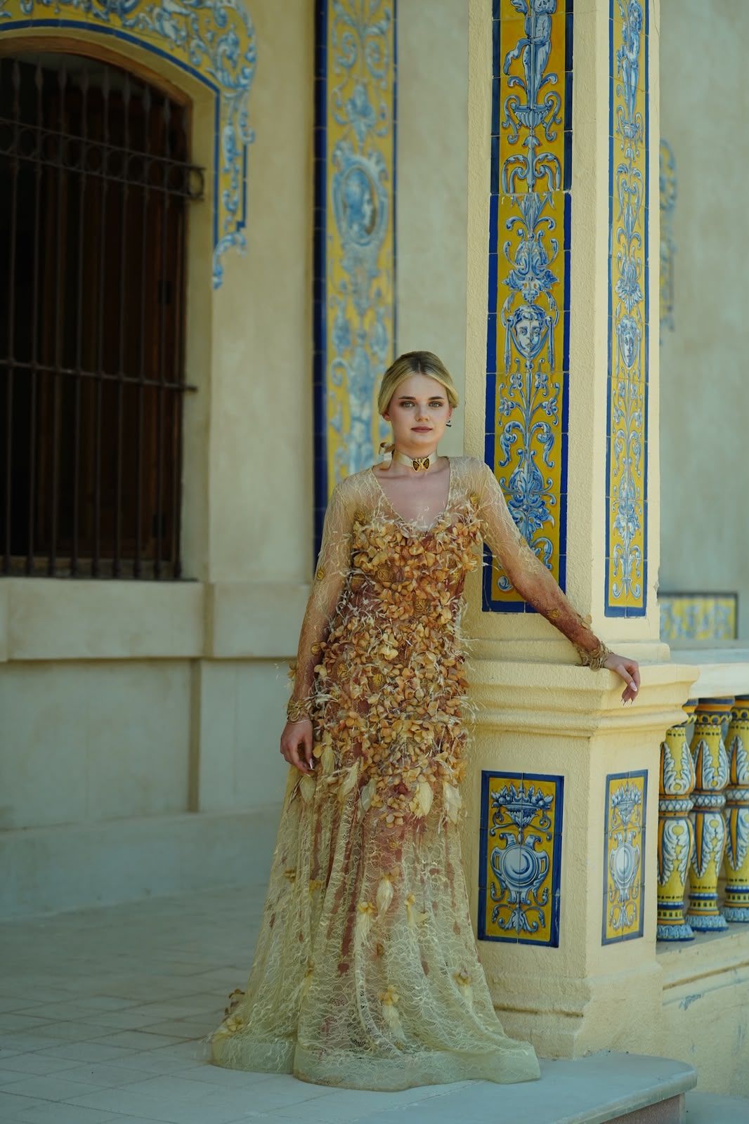 Vestido Ámbar de encaje y pétalos ante una columna de azulejo
